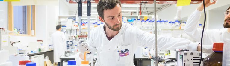 A male scientist in a white lab coat works in a lab.